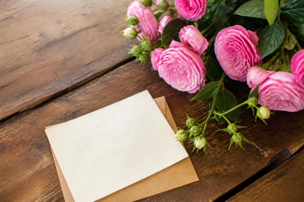 Carte manuscrite et fleurs roses sur table en bois